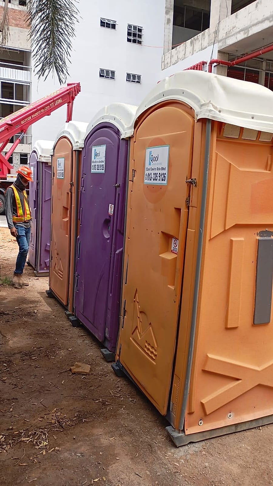 EQool portable toilets beside a building under construction with a worker in a hard hat