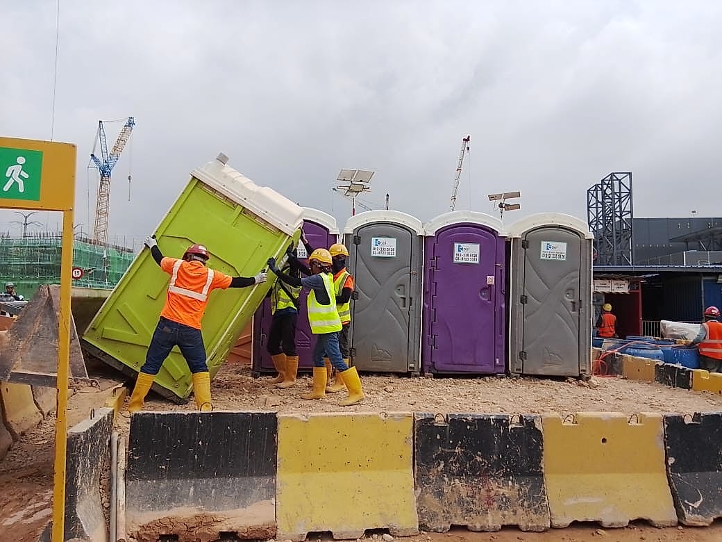 EQool crew members tilting a portable toilet upright beside a row of installed units on a construction site