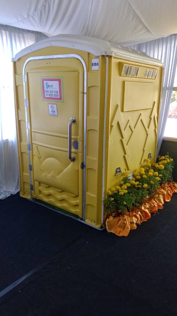 Yellow EQool VIP portable toilet inside a draped tent at the Borneo Flora Festival, with marigolds beside it