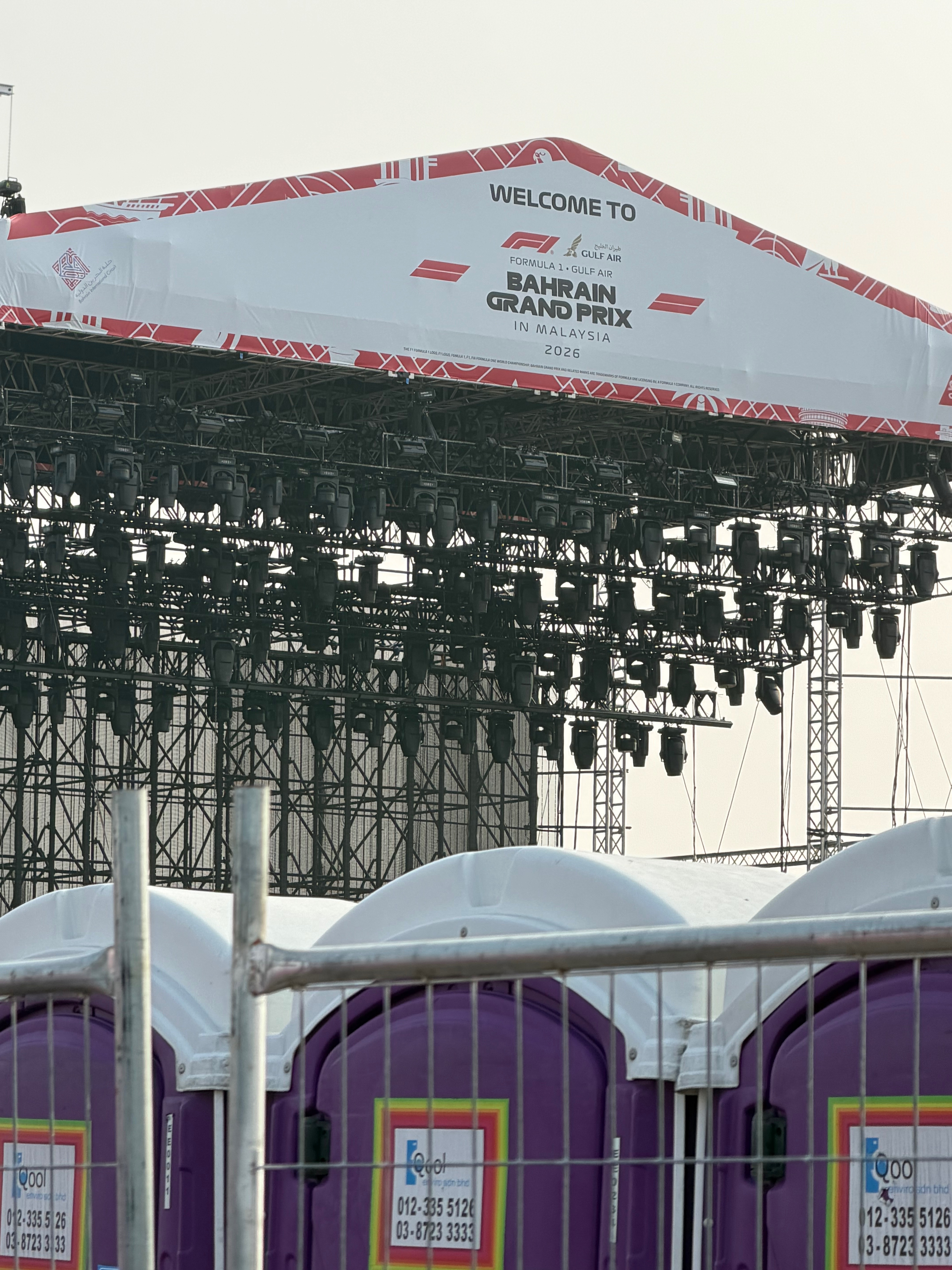 Main stage roof reading Welcome to Formula 1 Gulf Air Bahrain Grand Prix in Malaysia 2026, with EQool purple toilets behind a fence in front