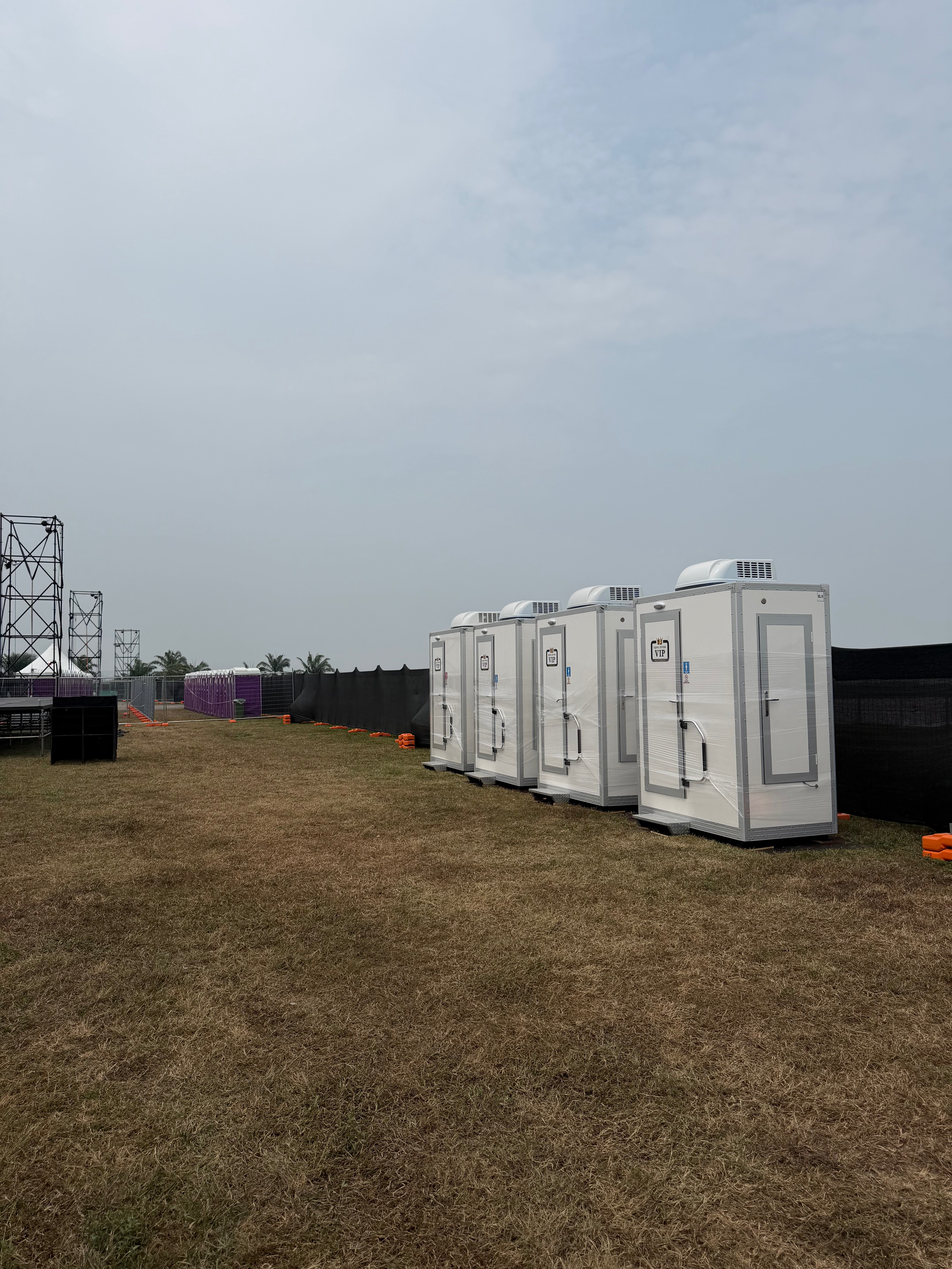 Four white EQool VIP cabin toilets with roof air-conditioning units on the grass beside the circuit