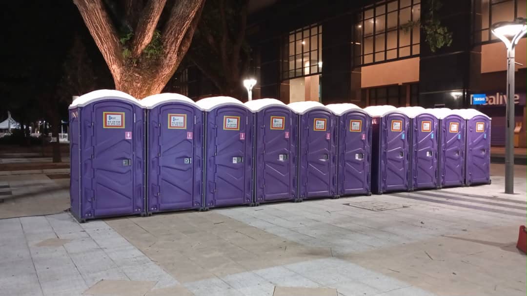 Row of purple EQool portable toilets lit by street lamps in an urban plaza at night, ready ahead of the National Day ceremony