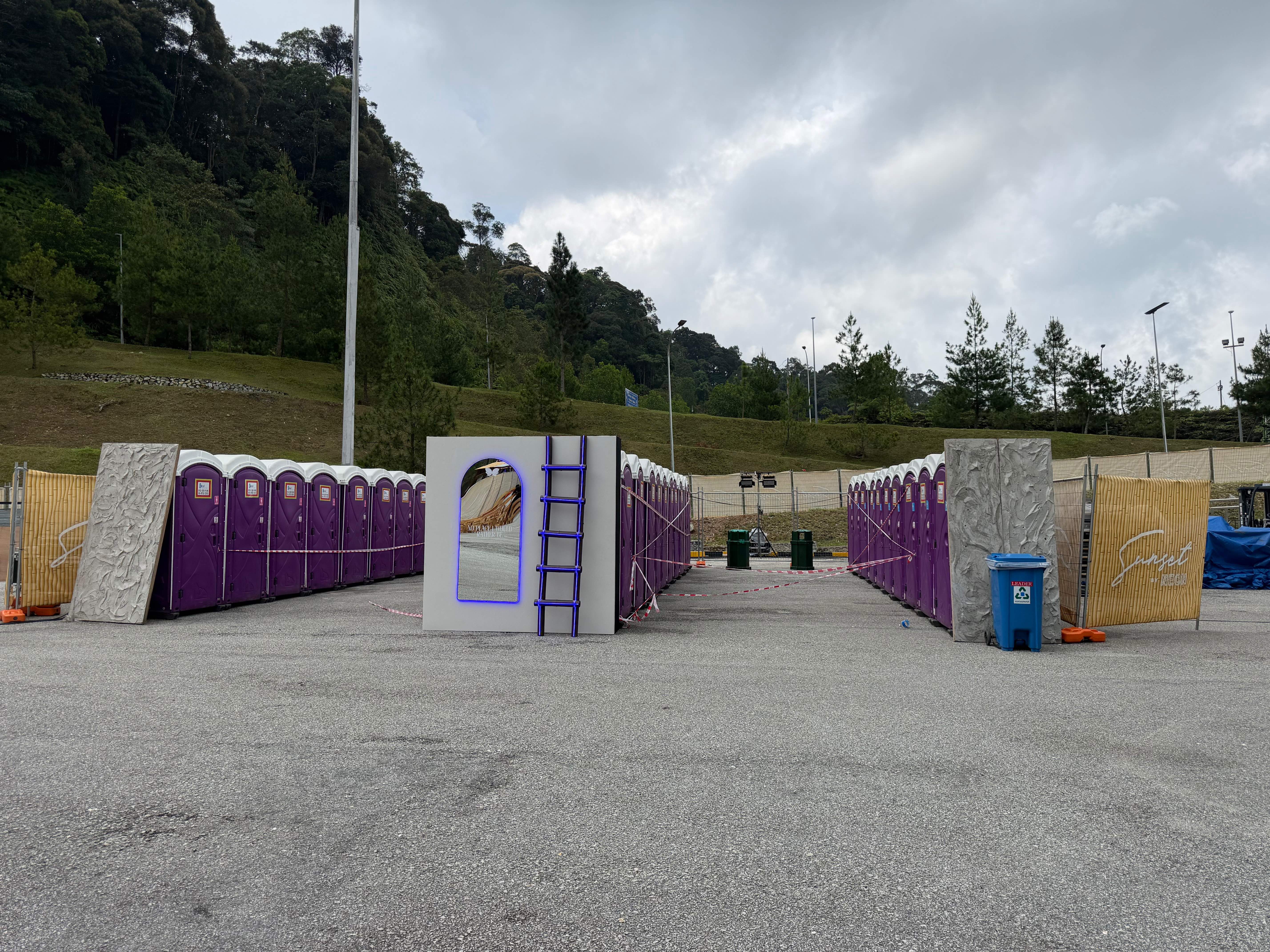 Two long rows of purple EQool portable toilets facing each other with a mirror and ladder photo wall between them at Sunset by NEON 2026